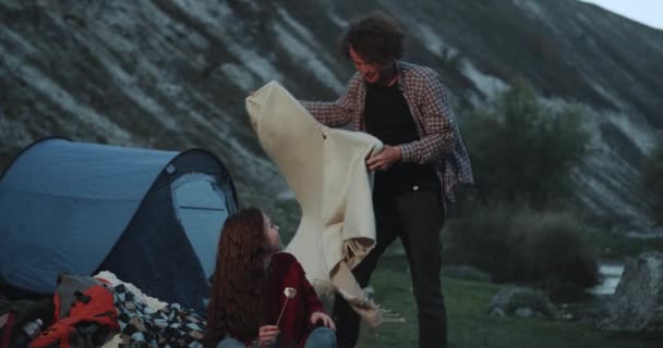 Noche perfecta para una pareja romántica, el tipo trae una manta para su novia y abrazándola muy romántica, se sientan al lado de una fogata en la montaña, comiendo malvaviscos . — Vídeo de stock