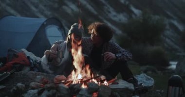 Closeup şaşırtıcı kamp ateşi güzel çift birbirlerine sarılma ve birlikte romantik vakit sıcak içecek bir şeyler içer.