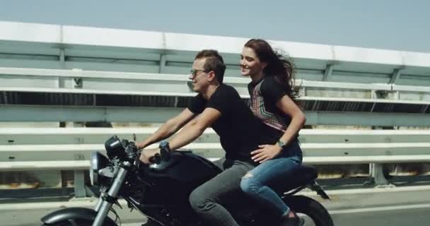 En el día ventoso de verano pareja joven tienen un paseo con una gran motocicleta negra en la autopista, señora feliz disfrutando del momento, chico con gafas de sol conduciendo la bicicleta . — Vídeos de Stock