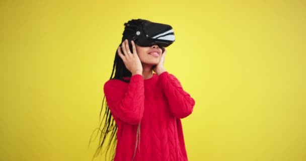 Afrikanska ung kvinna i en studio med en gul bakgrund som dansar roligt på samma gång hon använder en virtual reality-glasögon — Stockvideo