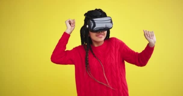 Очень красивая африканская леди, использующая VR движущуюся харизматичную танцевальную машину в студии с жёлтым фоном, она наслаждается временем в очках виртуальной реальности — стоковое видео