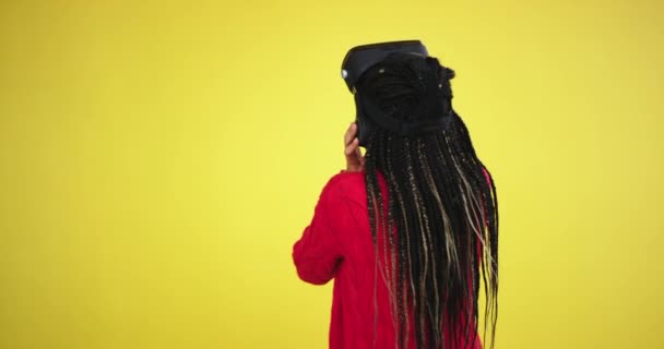 В студии с желтым фоном мульти этнической леди, с длинными волосами дреды энтузиазмом исследуя игру или путешествуя через очки виртуальной реальности — стоковое видео
