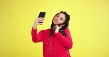 Karizmatik çok etnik Bayan selfies ile onun smartphone alarak bir sarı arka plan duvar ile stüdyoda o aynı zamanda poz almak fotoğraf önünde bir beyaz dişler ile büyük bir gülümseme var