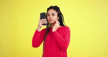 Çok dikkatli bir şekilde yüzüne bakıyor kamera önünde sarı arka plan duvar ile stüdyoda onu kendine ait bir fotoğraf çekmek için onun smartphone kullanılması ve oldukça poz güzel Afrikalı genç bayan
