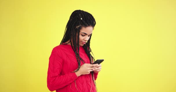 Zeer mooie en charismatische Afrikaanse ladyin de studio met een gele achtergrond met behulp van een smartphone en iets, voor de camera te typen — Stockvideo