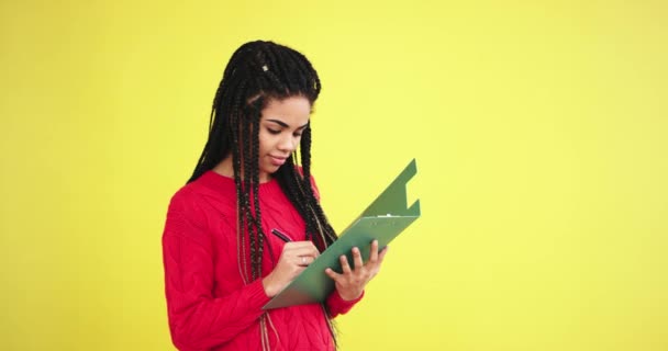 Trabalhador de escritório bonito em um estúdio com uma parede de fundo amarelo usando um mapa de escritório para fazer algumas notas, em seguida, curiosamente pensando em algo na frente da câmera — Vídeo de Stock