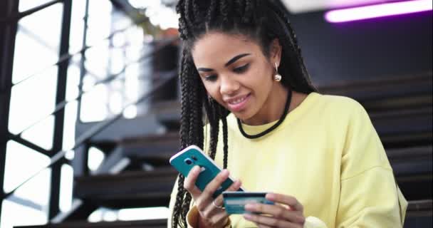 Πορτρέτο μια όμορφη χαρισματική αφρικανική νεαρή γυναίκα χρησιμοποιώντας το smartphone, να αγοράσουν ή να ελέγξετε κάτι χρήση της τραπεζικής κάρτας, πληκτρολογώντας τις λεπτομέρειες σχετικά με το τηλέφωνό της, αυτή είναι χαρούμενος και χαμογελαστός μεγάλο, αυτή συνεδρίαση — Αρχείο Βίντεο