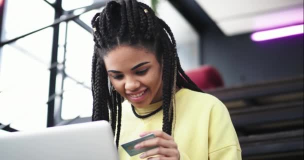 Zbliżenie wideo, biorąc z etnicznych Afryki ładna pani w sali urzędu, siedząc na schodach, zamówić coś z notebooka za pomocą karty płatniczej — Wideo stockowe