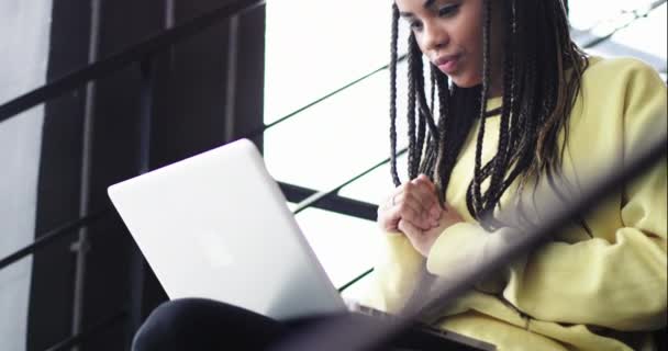 Détails rapprochés d'une employée de bureau femme africaine assise dans les escaliers et très concentrée regardant quelque chose sur son carnet — Video