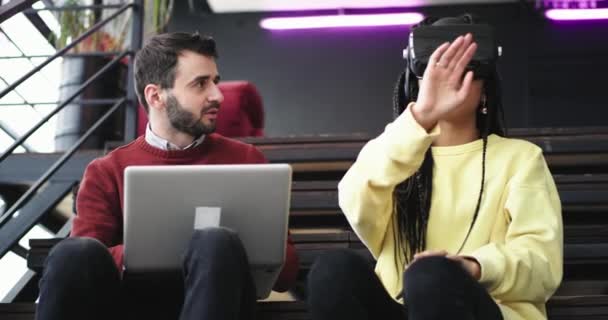 Belle immeuble de bureaux moderne deux employés de bureau ont une pause assis sur les escaliers et passer un drôle de moment ensemble dame africaine en utilisant une VR pour la première fois très impressionné elle explorer le — Video