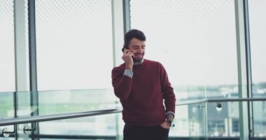 İyi görünümlü bir adam onun smartphone üzerinde yanında bir büyük pencere görünümünü konuşan bina bir işletmede.
