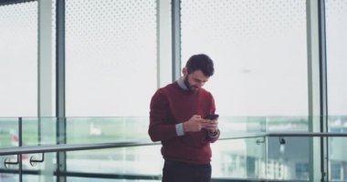 Genç işadamı bazı mesajları yazmak için onun smartphone kullanarak iyi bir ruh hali, o bir modern işletme binası büyük bir pencerede yanında duran bulunmaktadır. Kırmızı epic vurdu. 4k