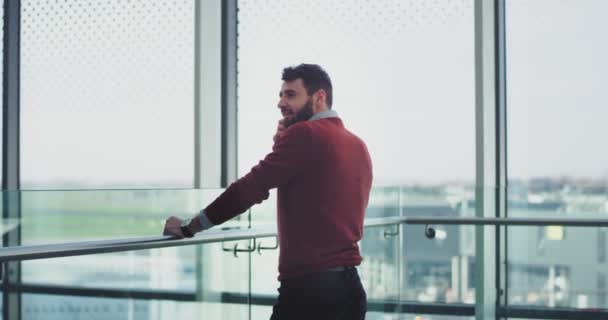 Businessman have a conversation on his smartphone in the airport , he are in a good mood , standing beside of a big window view. — Stock Video