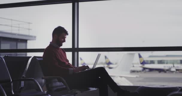 In de luchthaven stoelen zakenman te typen op zijn laptop tot hij wachten voor het vliegen, hij zijn zeer tevreden en genieten van de tijd. — Stockvideo