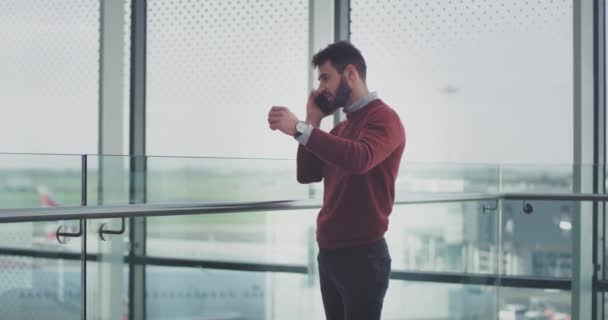 Бизнесмен в аэропорту ждет свою ширинку, он звонит кому-то, чтобы поговорить в конце он проверяет время на его руке часы — стоковое видео