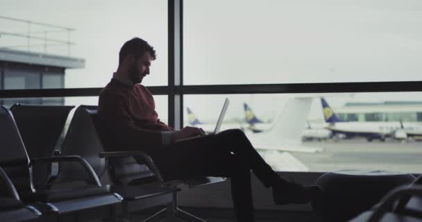Młody biznesmen na lotnisku siedząc na krześle i czeka na jego pokład pracował na jego laptopie bardzo entuzjastycznie. 4 k .shot na red epic. powolne ruchy — Wideo stockowe
