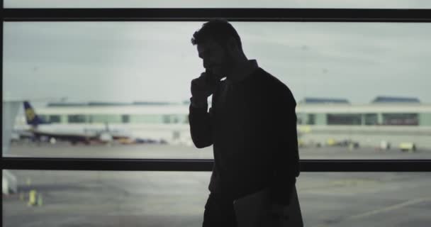 Närbild ung kille på flygplatsen i väntrummet hålla sin laptop och tala på sin telefon tills han kommer få ombordstigning — Stockvideo