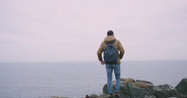 Νεαρός άνδρας στην κορυφή των βράχων μεγάλο βουνό θαυμάσει όλα το τοπίο γύρω, φόντο θέα στον ωκεανό, στη μέση της Ιρλανδίας. — Αρχείο Βίντεο