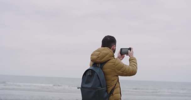 Deniz manzaralı geniş kumsalda genç adam turist geldi, o onun smartphone ile yer ve fotoğraf çekmek çok mutlu — Stok video