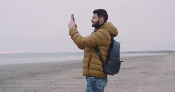 彼は広いビーチと美しい海の景色の美しい場所に到着した驚くべき国アイルランドで旅行する若い人は、風景の写真を撮る — ストック動画