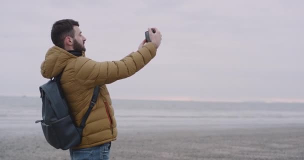 In de Ierse jonge kerel gelukkig aangekomen in fantastische plek in een groot strand met uitzicht op zee, toeristische nemen foto's van de plaats — Stockvideo