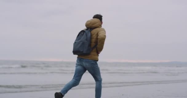 Correndo turista feliz na praia ao lado da praia, ele pulando na areia molhada — Vídeo de Stock