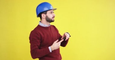 Bir şey kamera önünde smartphone kullanarak fotoğraf bir sarı arka plan duvar çekmek ile stüdyoda mavi bir kask ile genç mühendis. 4k