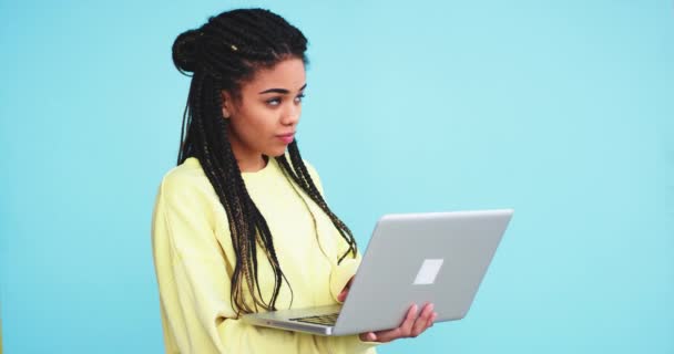 Em um estúdio com uma parede de fundo azul senhora africana digitando em seu caderno ou fazer uma pesquisa na internet, ela está muito entusiasmada — Vídeo de Stock