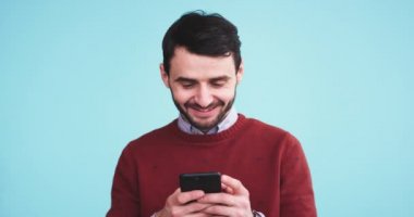 Bir mavi arka plan duvar ile bir stüdyoda bir mesaj yazmak için onun smartphone kullanarak kamera önünde mutlu ve gülümseyerek karizmatik adam