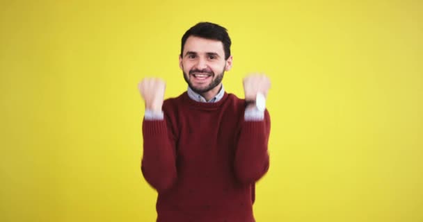 Sorrindo grande jovem na frente da câmera feliz e animado gesticulando com as mãos que ele começa algo que ele quer no estúdio com uma parede de fundo amarelo . — Vídeo de Stock