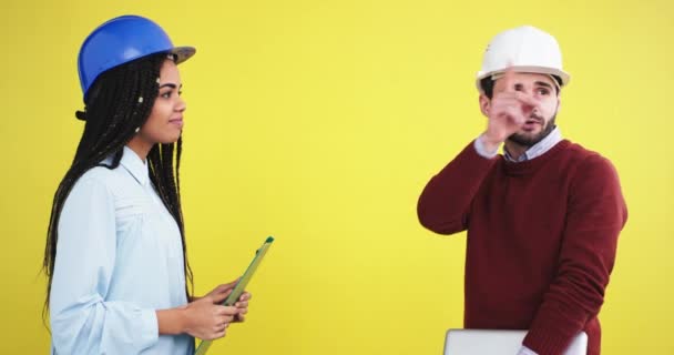 En el estudio con una pared de fondo amarillo una arquitecta africana étnica y un ingeniero con un casco azul hacen un trato frente a la cámara. 4k — Vídeos de Stock