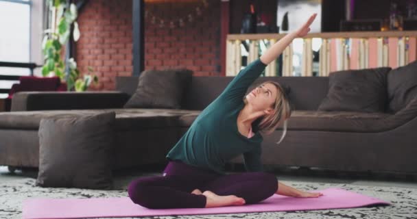 In living room modern design blonde lady practicing flexible yoga poses in the morning on the mat, she have meditation time for herself — стоковое видео