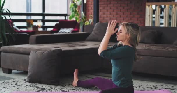 Yoga esticando corpo jovem senhora com cabelo loiro praticando de manhã no tapete na cobertura moderna com uma grande vista da janela — Vídeo de Stock