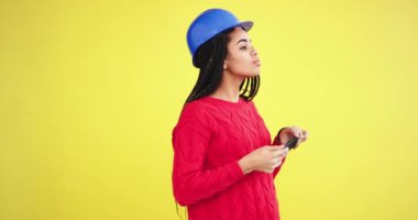 Güzel Bayan Afrika etnik bir sarı arka plan duvar ile stüdyoda yapmak resimleri whit onu smartphone, o mavi bir kask ve kırmızı bir kazak giyiyor.