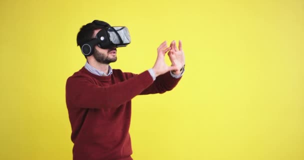 Muy curiosamente hombre usando unas gafas de realidad virtual y jugando un juego virtual que están muy impresionados de una realidad virtual en un estudio con una pared de fondo amarillo. 4k — Vídeos de Stock