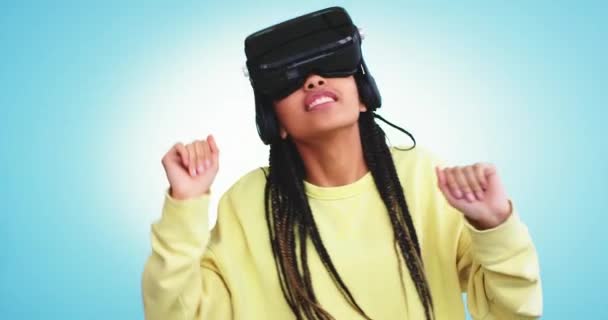 Dans un studio moderne avec un mur d'arrière-plan bleu et un flash sur le dos jeune femme africaine utilisant une VR pour jouer, elle est très heureuse et de bonne humeur — Video