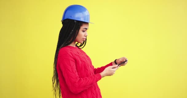 En serio joven ingeniera en un estudio con una pared de fondo amarillo tomando fotos usando su teléfono de construcción de imaginación. 4k — Vídeos de Stock