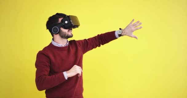 Smiling and happy young guy in a studio with a yellow background wall select the game virtual touching with finger, using a virtual reality glasses he are very impressed and excited of the game . — стоковое видео