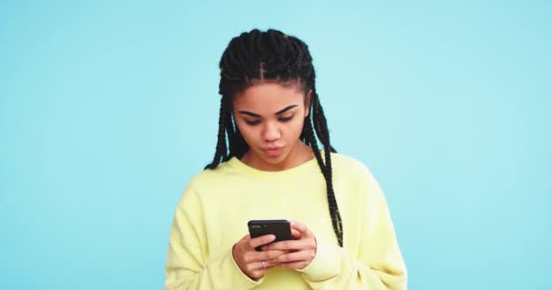 Зіткнувшись досить африканська леді смішно і усміхнено друкуючи на своєму смартфоні повідомлення в студії з синьою стіною фону — стокове відео