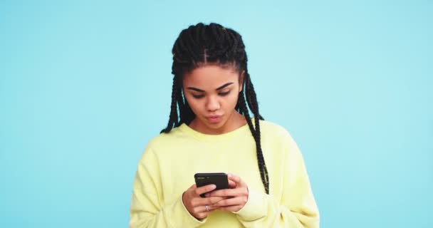 Dacing jolie dame africaine drôle et souriante tapant sur son smartphone un message dans le studio avec un mur de fond bleu — Video