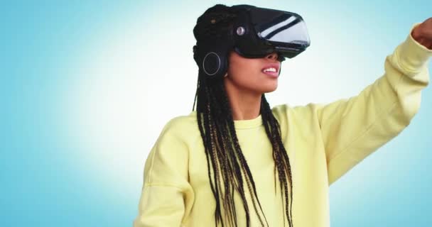 Multi senhora étnica com dreadlocks usando um óculos de realidade virtual para escolher um programa para usar virtual ela digitar com o dedo, muito entusiasmado em um estúdio com uma parede de fundo azul — Vídeo de Stock