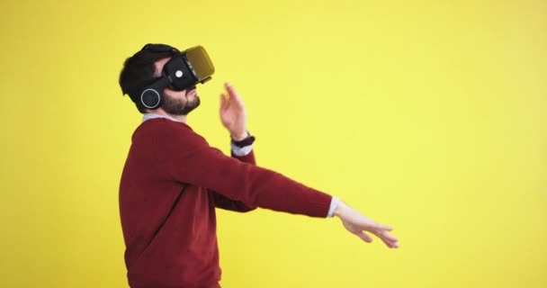 Смешной человек в очках виртуальной реальности, танцующий харизматично в студии с желтой стеной на заднем плане, он очень взволнован — стоковое видео