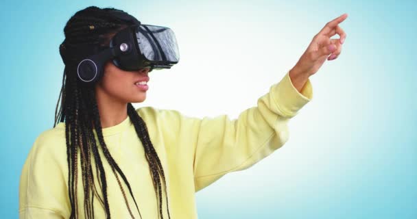 Nova tecnologia senhora africana com um VR digitando com dedo virtual para selecionar um programa para usar em um estúdio com uma parede de fundo azul — Vídeo de Stock
