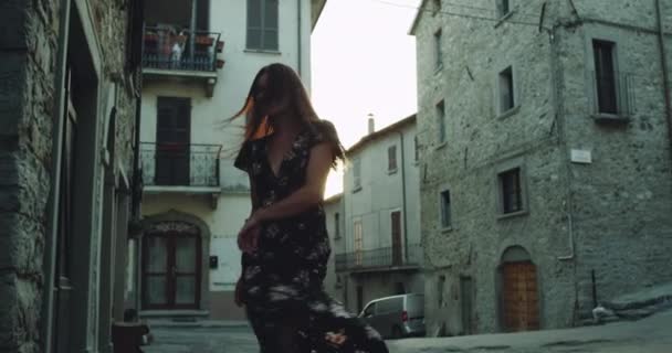 У молодой женщины есть набережная посреди улицы в Италии, она одета в длинное черное платье — стоковое видео