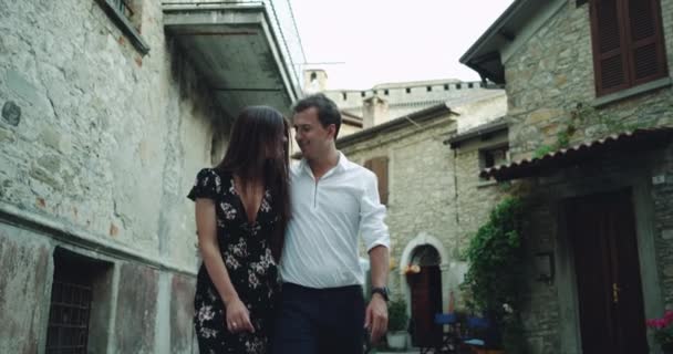 Romântico jovem casal bonito tem um passeio no meio de uma antiga rua italiana, eles olham um para o outro sorrindo e se divertir juntos . — Vídeo de Stock