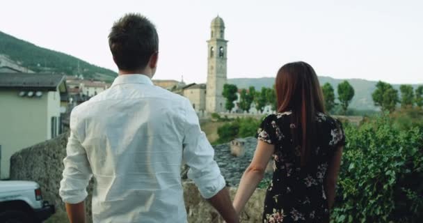 Casal jovem bonito romântico que refrigera abaixo da rua velha em Italy, pararam ao lado de uma cerca velha da pedra e abraçando e tocando romântico se — Vídeo de Stock