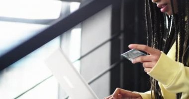 Bir kadın Afrika etnik ayrıntılarını modern bir ofis içinde kredi kartını ve ödeme için defterini kullanarak çevrimiçi bir işlem yapmak