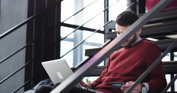 Stijlvol kantoor werknemer maken een transactie online met behulp van een credit card en een laptop gelukkig hij lachend grote aan het einde — Stockvideo