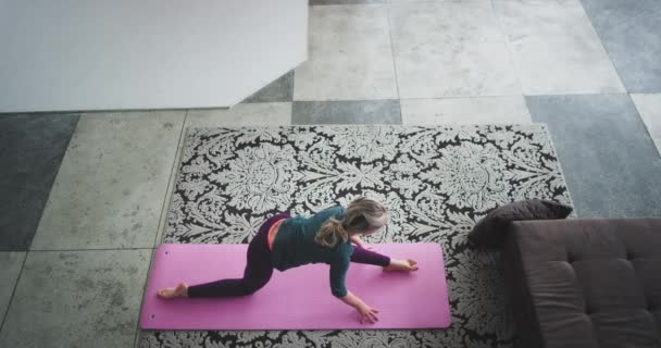 Desde la parte superior de la captura de vídeo de una señora que practica yoga en casa en la sala de estar en la estera, ella hace ejercicios duros y posa . — Vídeos de Stock