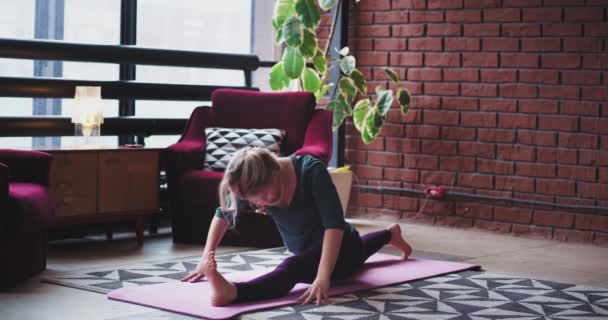 Esticando o corpo na manhã jovem em casa ela faz poses de ioga no tapete na sala de estar com design moderno e parede de estilo urbano — Vídeo de Stock